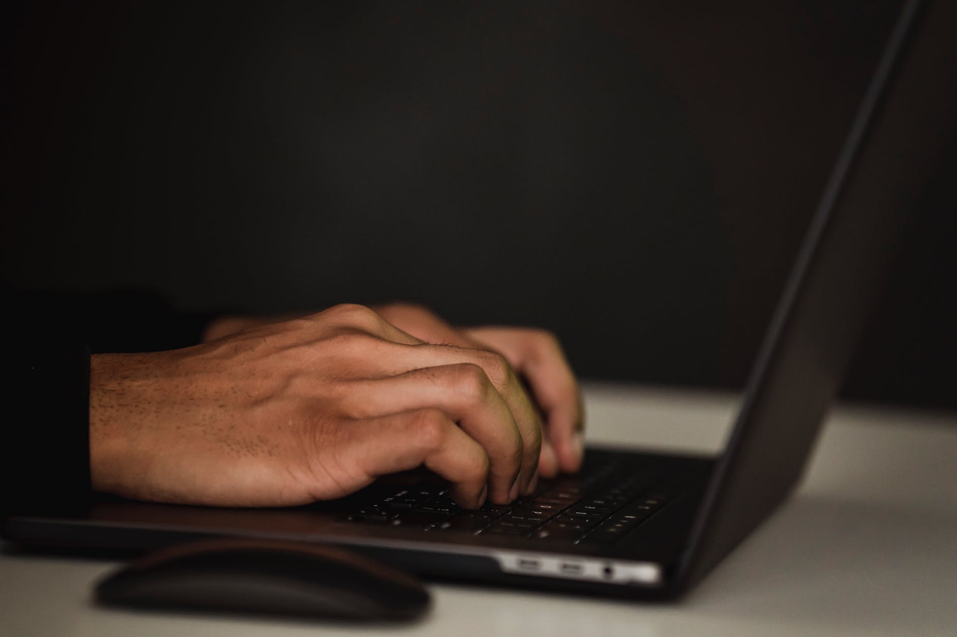 crop faceless person using laptop in darkness